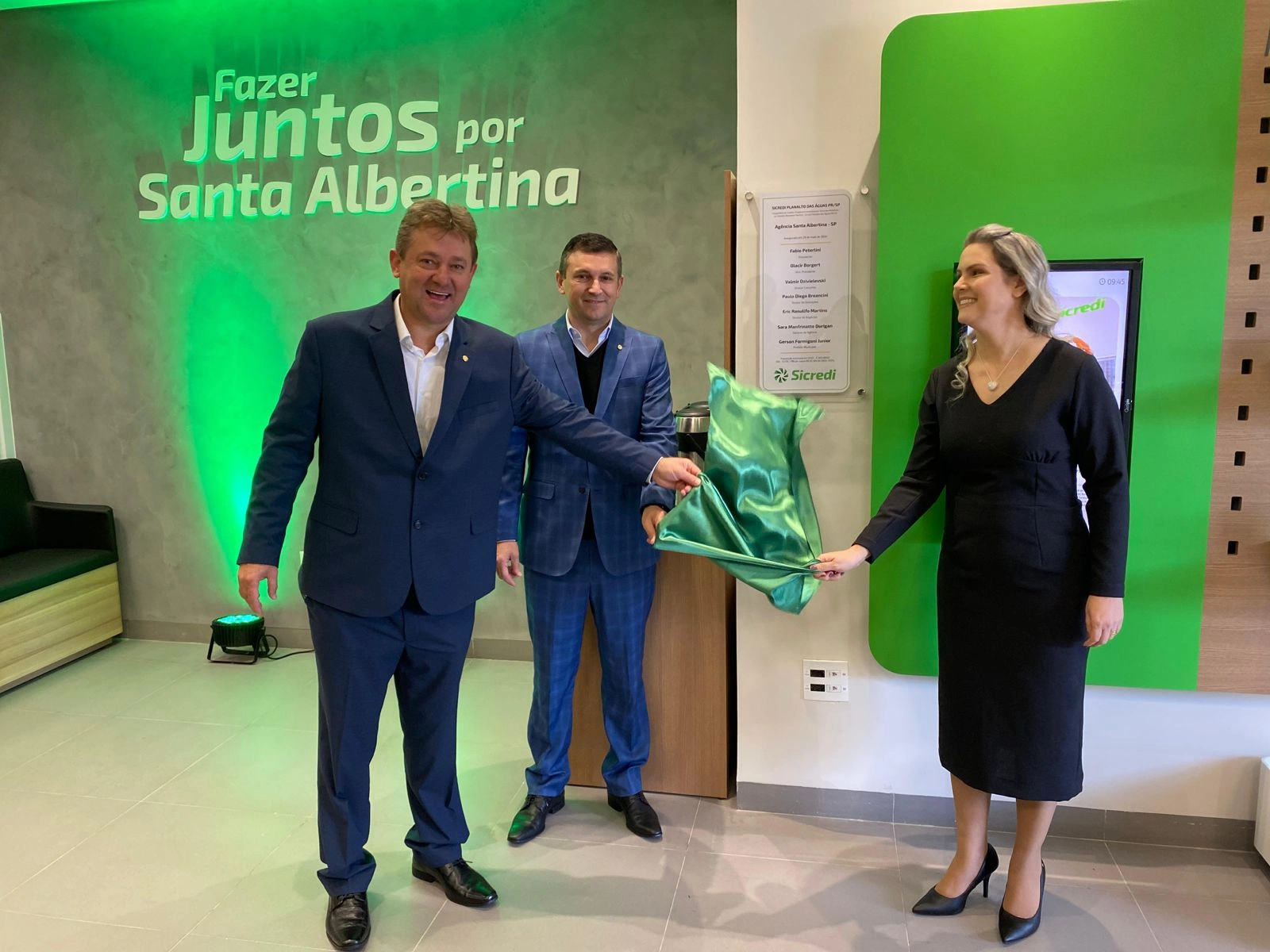  Pessoas com roupas formais retirando o tecido da placa de inauguração 