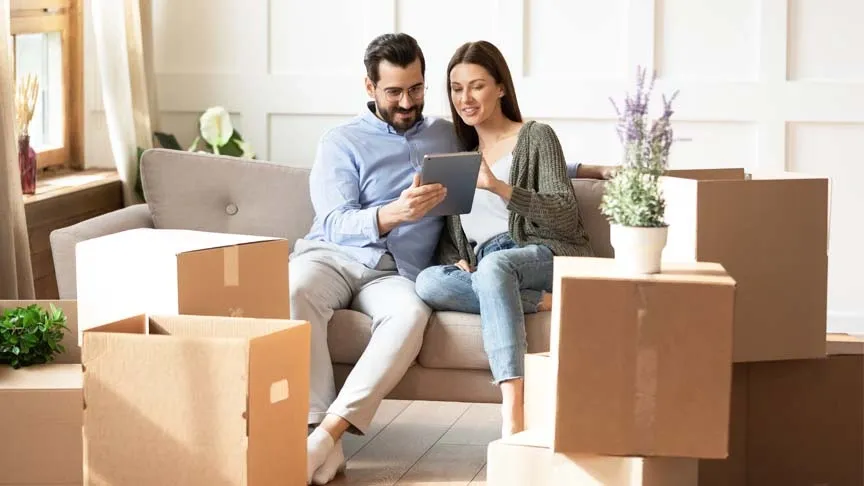  Casal em sofá, ao lado de caixas de mudança, olhando para um tablet. 