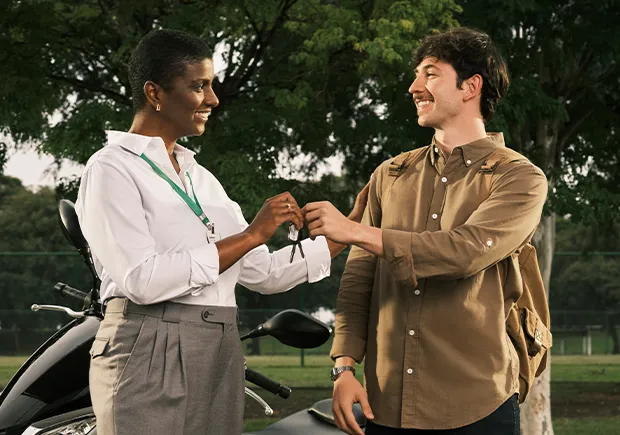  Homem jovem recebendo as chaves de uma moto das mãos de uma gerente negra do Sicredi. 