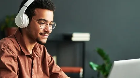  Rapaz negro de pele clara sorridente com fones no ouvido e olhando para o computador 