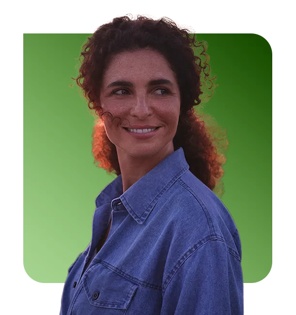  Pessoa usando camisa jeans em uma plantação, com um trator ao fundo em uma estrada de terra. O céu está colorido pelo pôr do sol, com tons de laranja, rosa e roxo. 