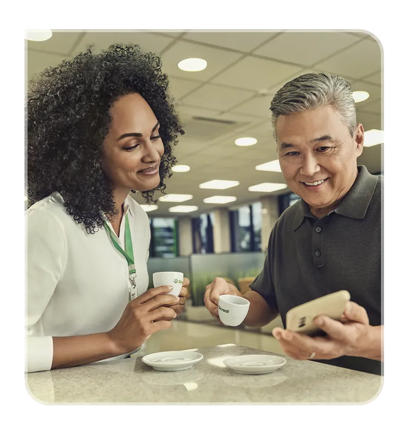  Um associado segurando o celular enquanto a gerente olha com felicidade segurando uma xícara de café. 