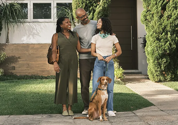  família reunida em frente a casa com pai, mãe, filha e cachoro 