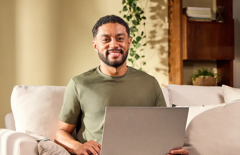  Homem negro de pele clara com notebook na perna, sorrindo e olhando pra câmera 