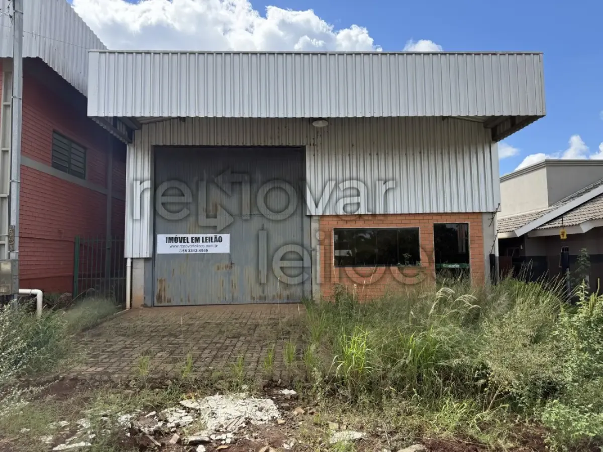  Fachada frontal de galpão de uso industrial ou comercial em Ibirubá (RS), com estrutura metálica, fechamento em chapas metálicas, portão de grandes dimensões para acesso de veículos, base em alvenaria e área externa pavimentada. 