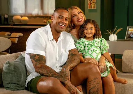  Leo Santana, Lore Improta e filha sorriem em sofá em casa. 