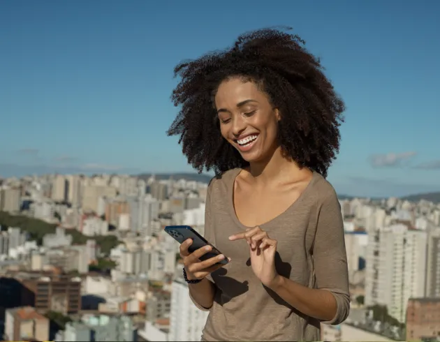  mulher negra sorri com celular nas mãos 