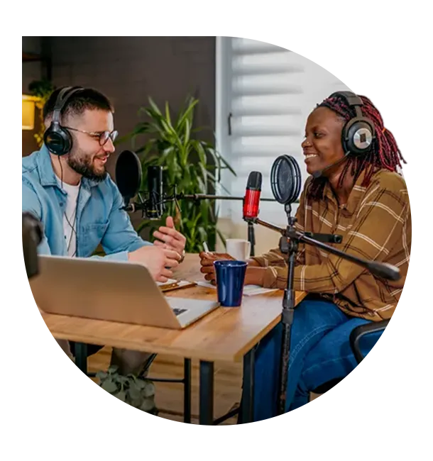  Duas pessoas gravam conversa em formato de podcast, com microfones e fones de ouvido, em ambiente interno com notebook sobre a mesa. Cena representa colaboração, diálogo e proximidade no atendimento, alinhados aos valores do cooperativismo Sicredi. 
