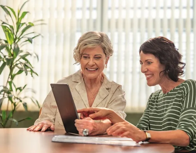  duas mulheres de mais de 50 anos sentadas numa mesa olhando a tela de um computador 