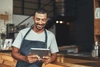  homem empreendedor de camiseta cinza, avental cinza e segurando um tablet 