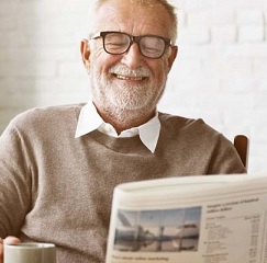 Homem idoso lendo jornal enquanto toma café