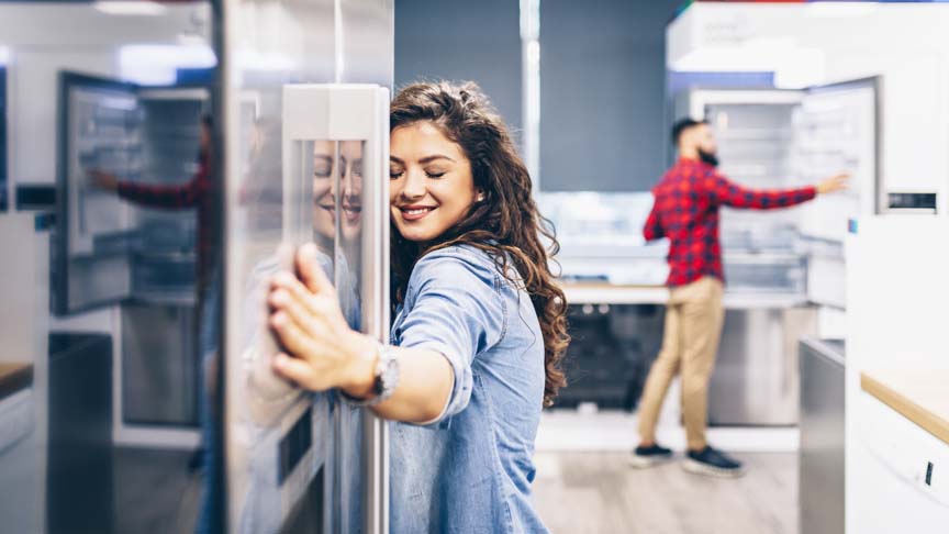 Mulher feliz abraçada na geladeira em uma loja de eletrônicos