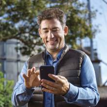 Imagem de um homem sorrindo e utilizando o celular