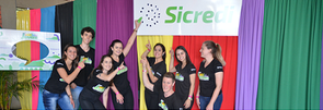 Integrantes do Comitê Jovem apontando para a marca do Sicredi em fundo colorido