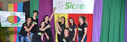 Integrantes do Comitê Jovem apontando para a marca do Sicredi em fundo colorido