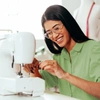  Mulher utilizando uma máquina de costura e sorrindo - Seguro empresarial Sicredi 