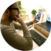  Homem sentado em frente ao computador e com um telefone celular na mão esquerda 