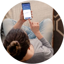  pessoa vista de cima, sentada em uma sofá e com manuseando o celular em mãos 