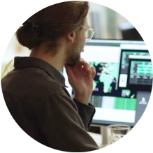  Pessoa de costas olhando para telas de computadores em cima da mesa. 