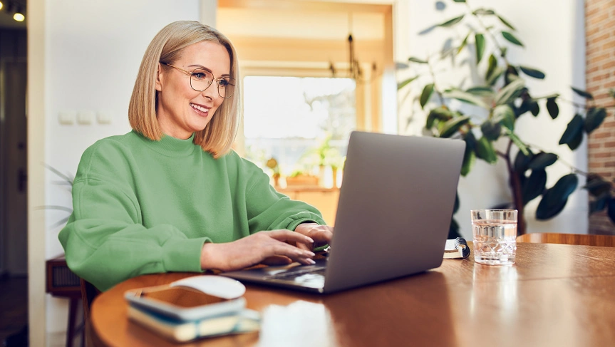  Mulher sentada em frente ao desktop programando pagamentos com débito automático Sicredi. 