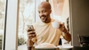  Homem sentado tomando café, segurando o seu smartphone e realizando seu pagamento com o Pix do Sicredi. 