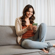  Menina sentada em sofá utilizando a recarga de celular do Sicredi. 
