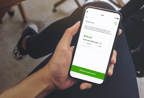  Mão de uma pessoa segurando um celular e na tela aparece o cartão virtual do Sicredi. 