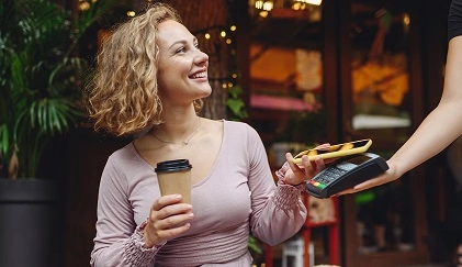  Mulher sentada com um café em mãos, fazendo seu pagamento com carteiras digitais Sicredi. 