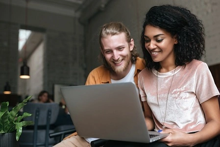  Homem e mulher usando computador para resgatar pontos do programa de recompensa dos cartões Sicredi 