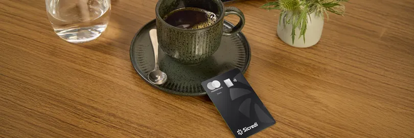 xícara de café escura com cartão Sicredi Mastercard Black ao lado