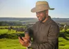  homem negro com chapéu no campo sorri olhando para celular 