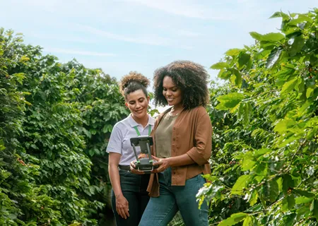 homem branco com chapéu posa em frente a trator e plantação