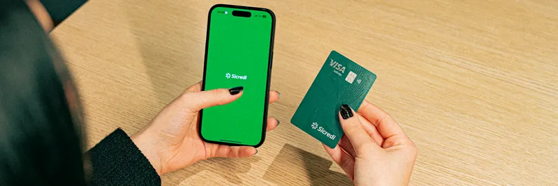  mulher segura celular e cartão Sicredi 