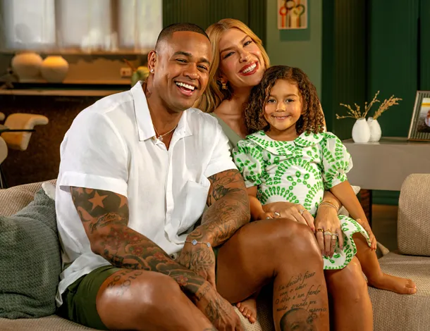 Leo Santana, Lore Improta e filha sorriem em sofá em casa