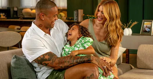 Leo Santana, Lore Improta e filha sorriem no sofá de casa