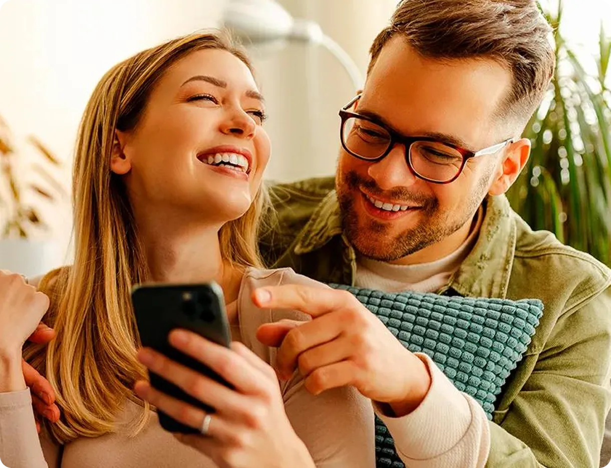  Duas pessoas observam juntas a tela de um celular enquanto uma delas aponta para o aparelho. 